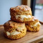 Close-up of stacked, glazed sweet potato biscuits sliced and filled with a thick, creamy filling.