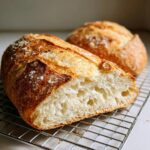 Close-up of a freshly baked french bread loaf cut in half, showing the airy interior crumb, resting on a wire rack.