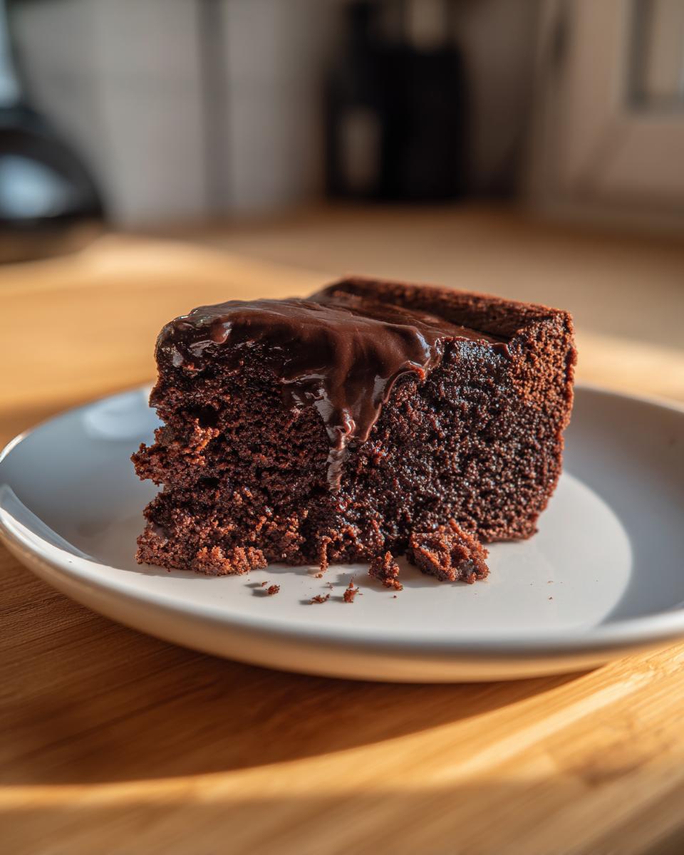 A rich, fudgy slice of flourless chocolate cake topped with melting chocolate ganache, served on a white plate.