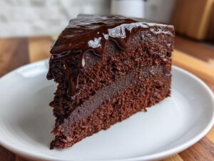 A rich, dark slice of fudgy flourless chocolate cake topped with glossy chocolate ganache dripping down the sides.