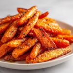 Close-up of a pile of beautifully glazed and seasoned roasted carrots on a light plate.