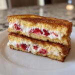 Two halves of golden brown stuffed french toast stacked, revealing a creamy filling mixed with sliced strawberries.