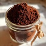 Close-up of a glass jar filled high with rich, dark brown homemade hot cocoa mix powder.