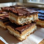 Two stacked squares of rich buckeye fudge showing a shortbread base, peanut butter layer, and chocolate topping.