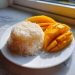 A serving of sweet sticky rice molded into a dome next to fresh, sliced mango, showcasing the classic mango sticky rice dessert.
