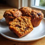 Close-up of moist bran muffins, one cut in half showing the texture and raisins inside.