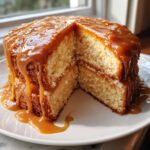 A two-layer moist caramel cake with a slice removed, generously topped and filled with thick, dripping caramel sauce.