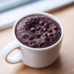 Close-up of a moist chocolate mug cake topped with chocolate chips, ready to eat.