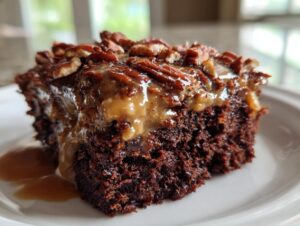 Close-up of a moist slice of german chocolate poke cake topped with gooey caramel and toasted pecans.