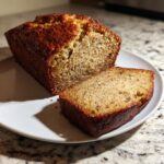 A golden-brown loaf of sugar free banana bread, partially sliced, showing a moist interior texture.