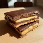 Two stacked no bake buckeye graham crackers featuring peanut butter filling and a rich chocolate coating.