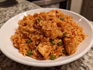 A close-up of a white bowl filled with seasoned rice, chunks of chicken, and green peas, representing the Cajun chicken recipe.