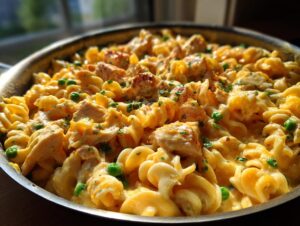 Close-up of creamy, cheesy tuna pasta with peas and chunks of protein in a stainless steel skillet.