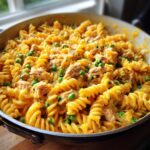 Close-up of creamy tuna pasta made with fusilli, tuna chunks, and bright green peas, served hot in a skillet.