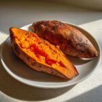 Close-up of a perfectly baked sweet potato, split open to show the bright orange, fluffy interior, seasoned with salt.