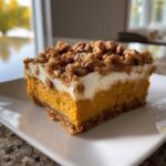 A rich, layered slice of pumpkin crunch dessert with a creamy topping and pecan crumble.