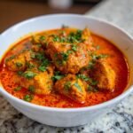 Close-up of tender chicken pieces swimming in a vibrant orange-red sauce, garnished with fresh cilantro, representing delicious butter chicken.