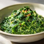Close-up of rich, vibrant green creamed spinach recipe topped with crispy brown bits in a light-colored bowl.
