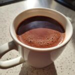 Close-up of a rich, dark french hot chocolate with a foamy top in a white mug.