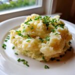 A generous scoop of creamy roasted garlic mashed potatoes topped with fresh, chopped green chives on a white plate.