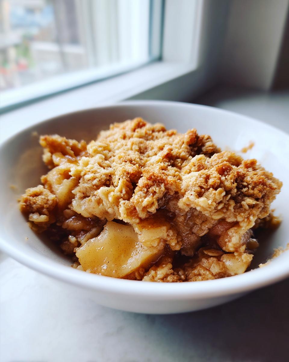 Close-up of a warm serving of apple crisp recipe with a crunchy oat topping in a white bowl.
