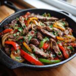 Close-up of sizzling steak fajitas with colorful peppers and onions in a black cast iron skillet.