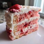 A tall slice of layered strawberry cake with white frosting and fresh strawberries.