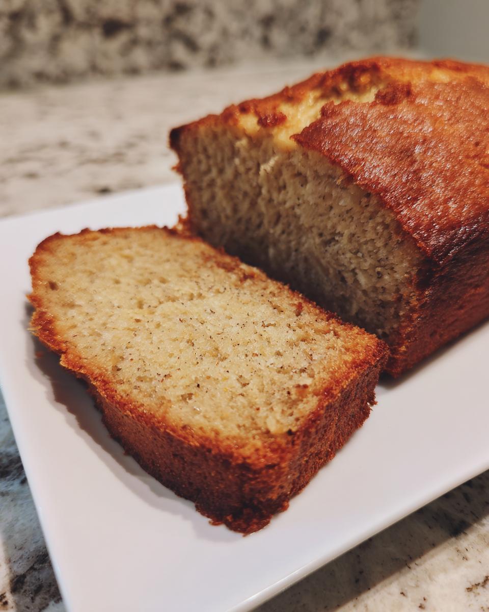 A thick slice cut from a loaf of moist sugar free banana bread, served on a white rectangular plate.