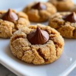A close-up of a soft, chewy peanut butter blossoms cookie rolled in sugar with a chocolate kiss pressed into the center.