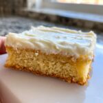 A close-up view of a single, soft sugar cookie bars square topped with thick white frosting.