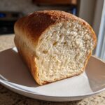 A freshly baked loaf of soft whole wheat bread, sliced to show the airy crumb structure, resting on a white plate.