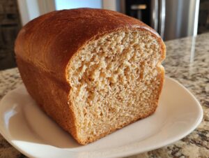 A freshly baked loaf of soft whole wheat bread, shown sliced to reveal its fluffy, light brown interior crumb.