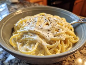 Close-up of spaghetti coated in rich homemade alfredo sauce, topped with cracked black pepper.