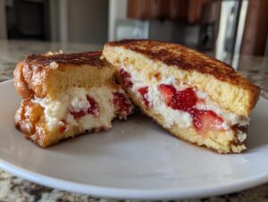 Close-up of strawberry stuffed french toast cut in half, showing creamy filling and golden-brown bread.