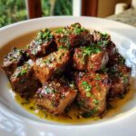 Close-up of tender crockpot steak bites glistening in garlic butter sauce and topped with fresh parsley.