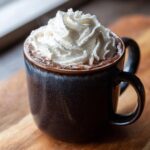 Close-up of a mug filled with thick hot chocolate, generously topped with swirls of whipped cream.