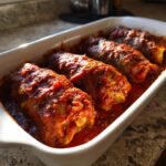 Four plump cabbage rolls simmering in a rich, bright red tomato sauce inside a white baking dish.