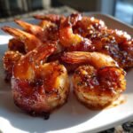 Close-up of several perfectly cooked, glazed bacon wrapped shrimp piled on a white plate.