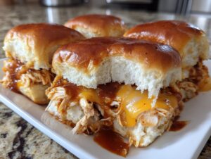 Close-up of four delicious bbq chicken sliders with melted cheese and sticky BBQ sauce on soft rolls.