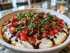 Close-up of a creamy white bruschetta dip topped with diced tomatoes, fresh basil, and balsamic glaze.