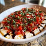 Close-up of a creamy white bruschetta dip topped with diced tomatoes, fresh basil, and a balsamic glaze drizzle.