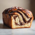 A golden-brown, freshly baked chocolate babka loaf showing beautiful swirls of rich chocolate filling.