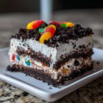 A layered slice of amazing dirt cake featuring cream, chocolate crumbs, and gummy worms on top.