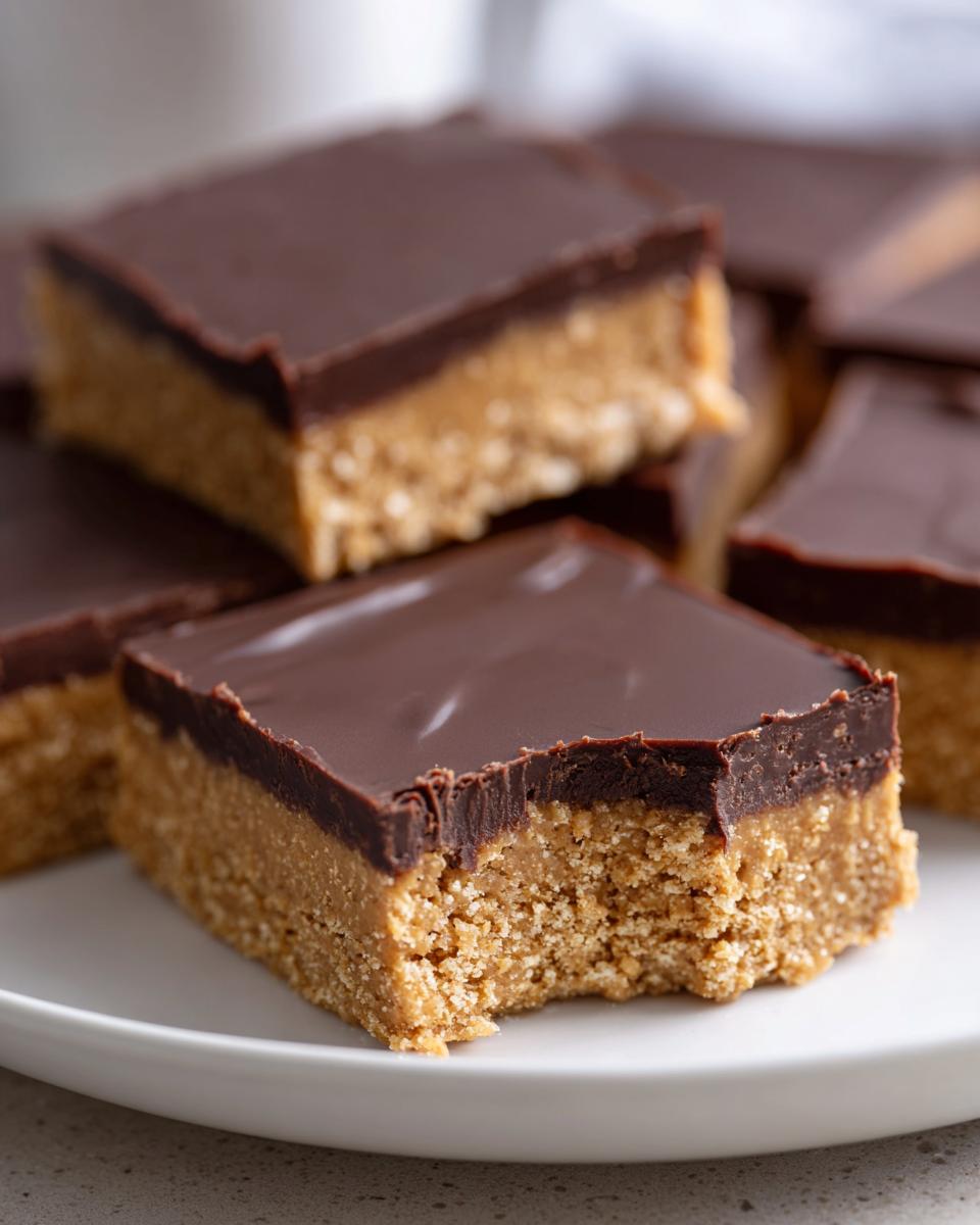 A close-up of delicious peanut butter bars stacked on a white plate, featuring a thick peanut butter base and a smooth chocolate layer on top.