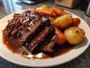 Close-up of shredded, tender pot roast covered in rich brown gravy, served alongside roasted carrots and potatoes.