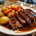 Slices of tender pot roast covered in rich brown gravy, served alongside roasted carrots and small potatoes.