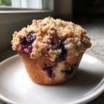 A close-up of a freshly baked blueberry muffins with a thick, golden streusel crumb topping.