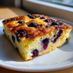 Close-up of a thick, golden-brown slice of blueberry sheet pan pancakes on a white plate.