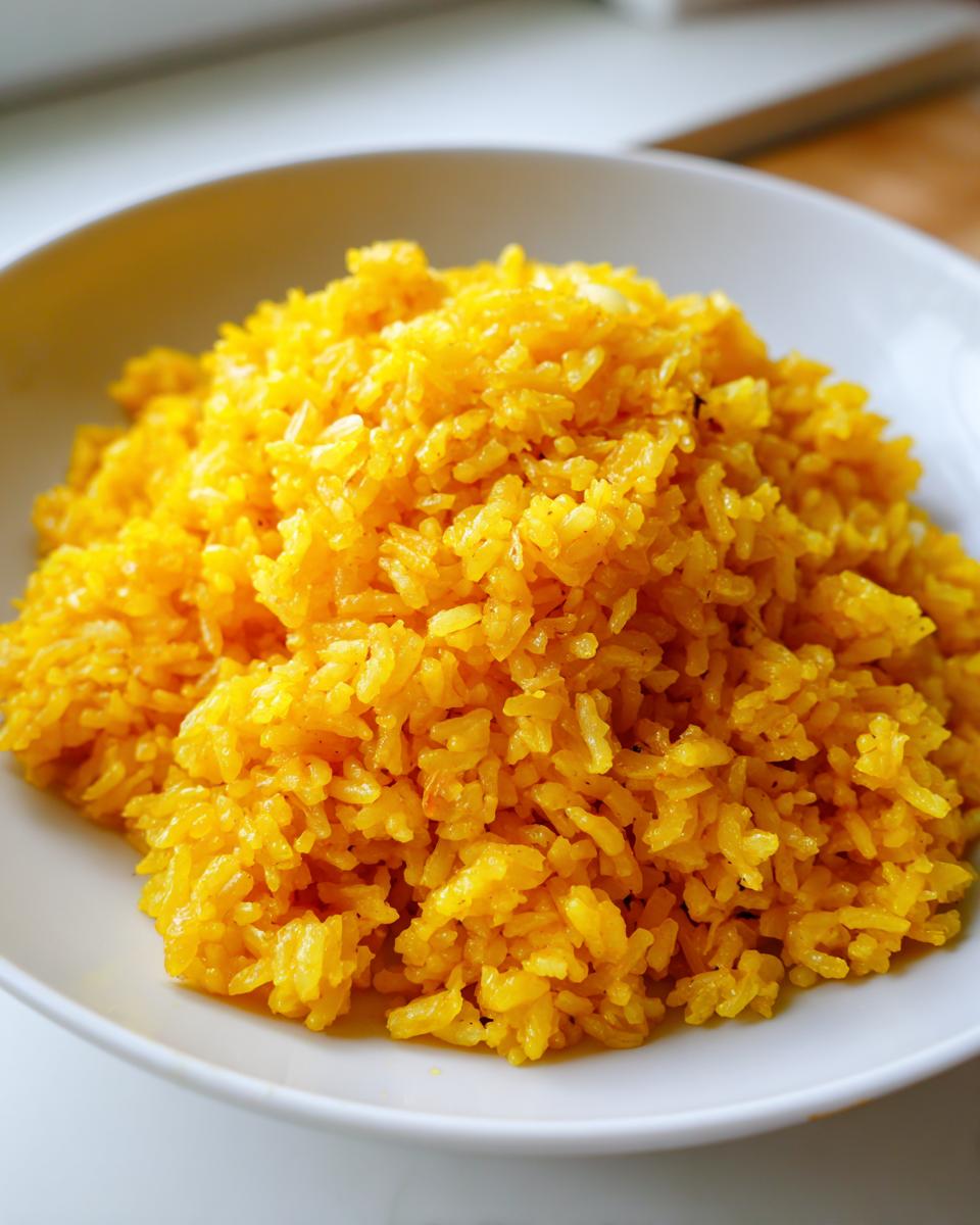 A close-up of fluffy, vibrant yellow turmeric rice served in a simple white bowl.