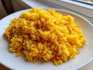 A serving of fluffy, bright yellow turmeric rice piled high on a simple white plate.